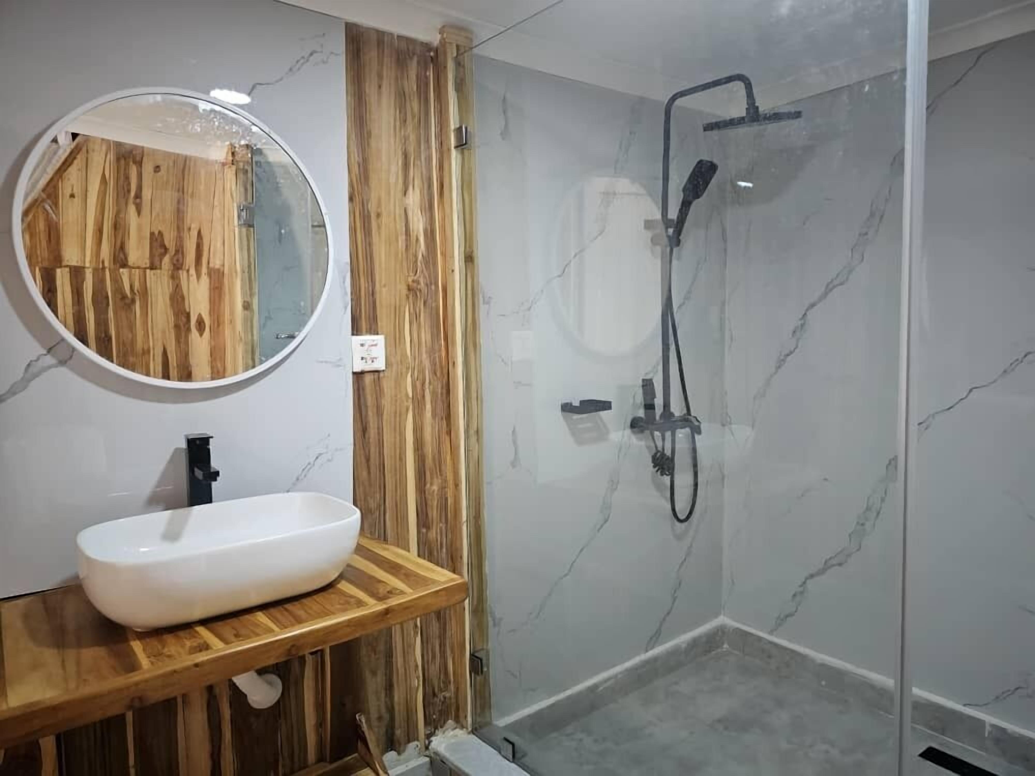 Une salle de bain avec un meuble-lavabo en bois, un miroir rond et une douche à parois de verre.