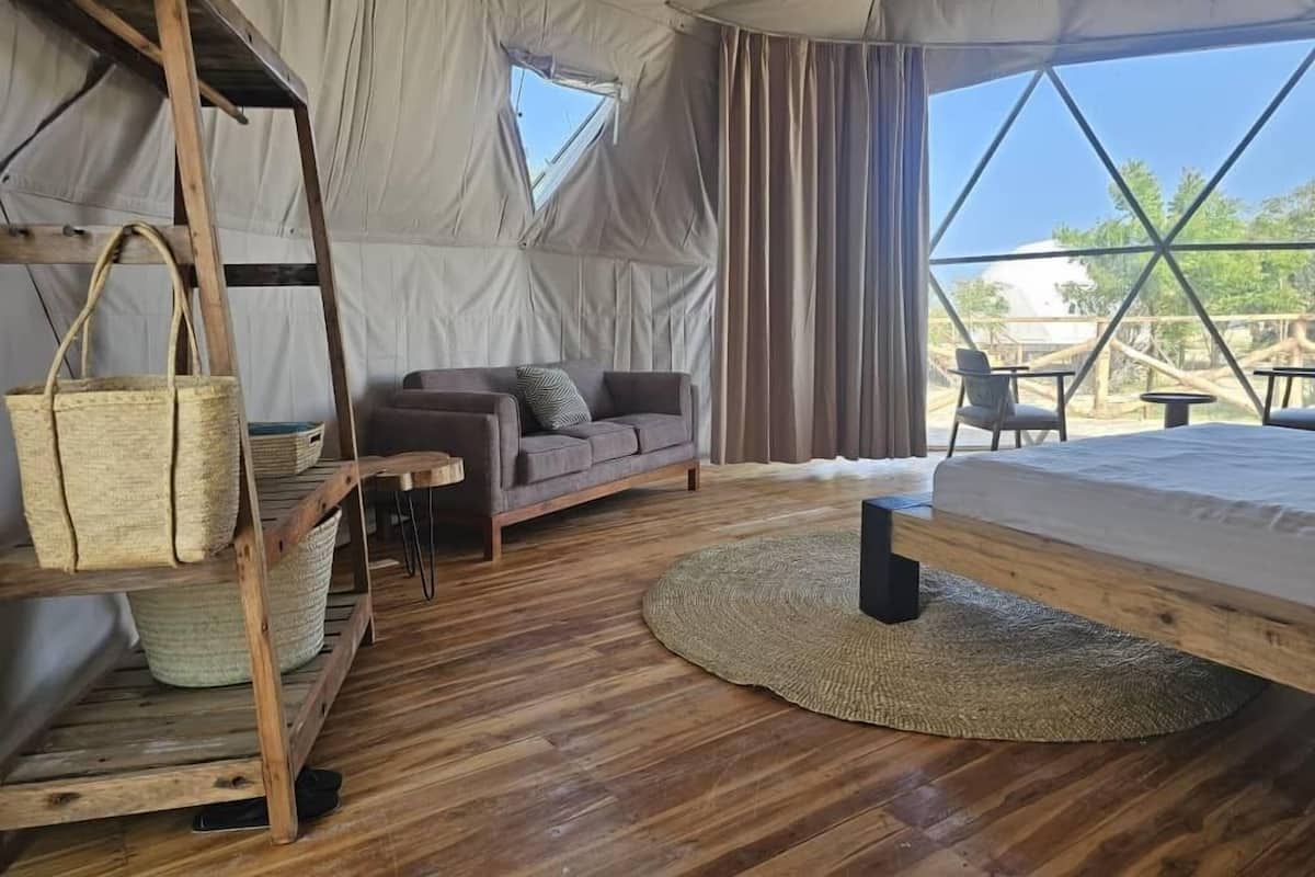 Un hébergement sous tente doté d’un plancher en bois, d’un canapé, d’un lit et d’un coin repas avec tables et chaises.