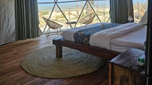 Una habitación con carpa, una cama, un tapete redondo tejido y vistas a la playa.
