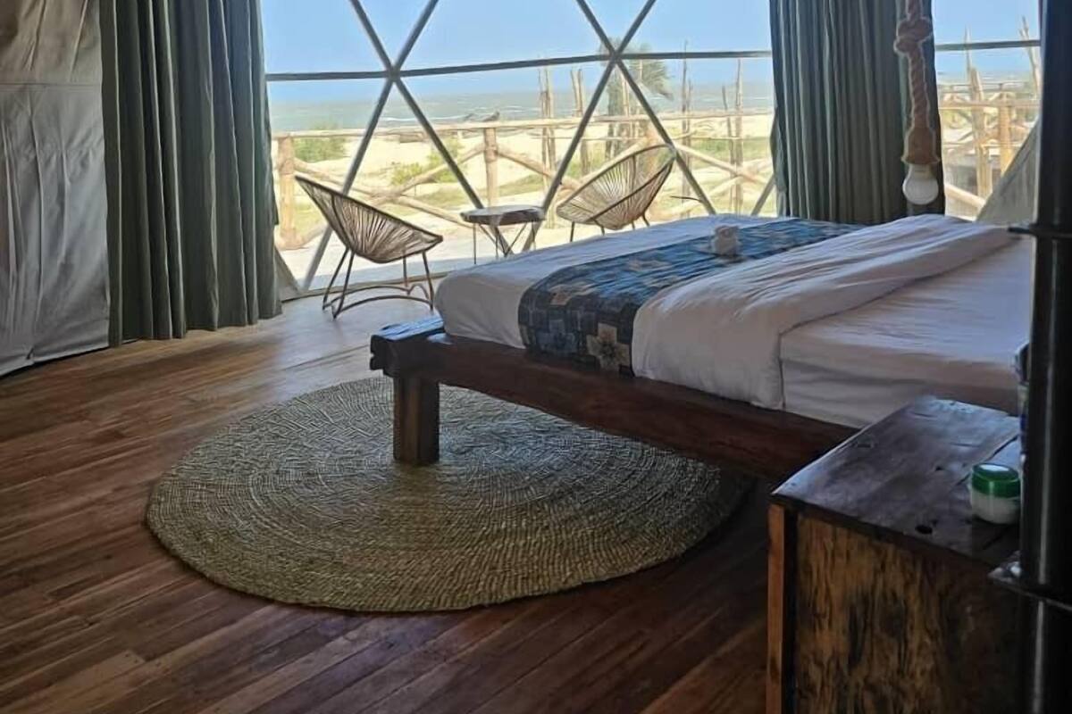 Une pièce aménagée avec une tente, un lit, un tapis rond tissé et une vue sur la plage.