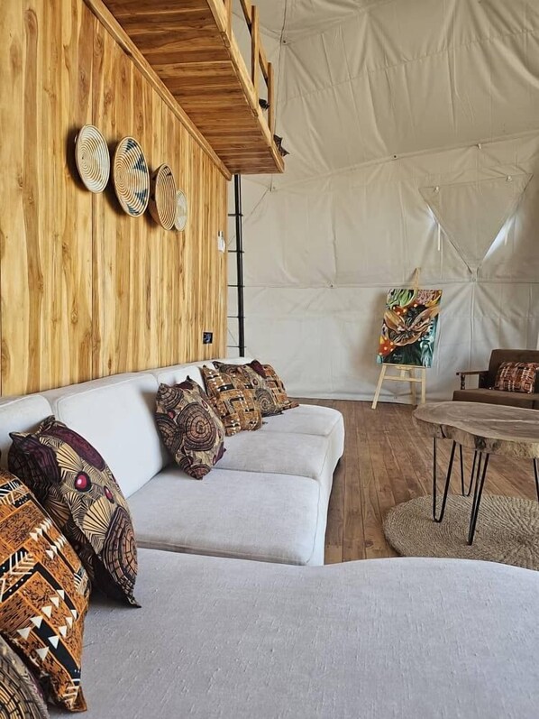 A tented room with a wooden wall, a white sofa with patterned cushions, and a round wooden table.