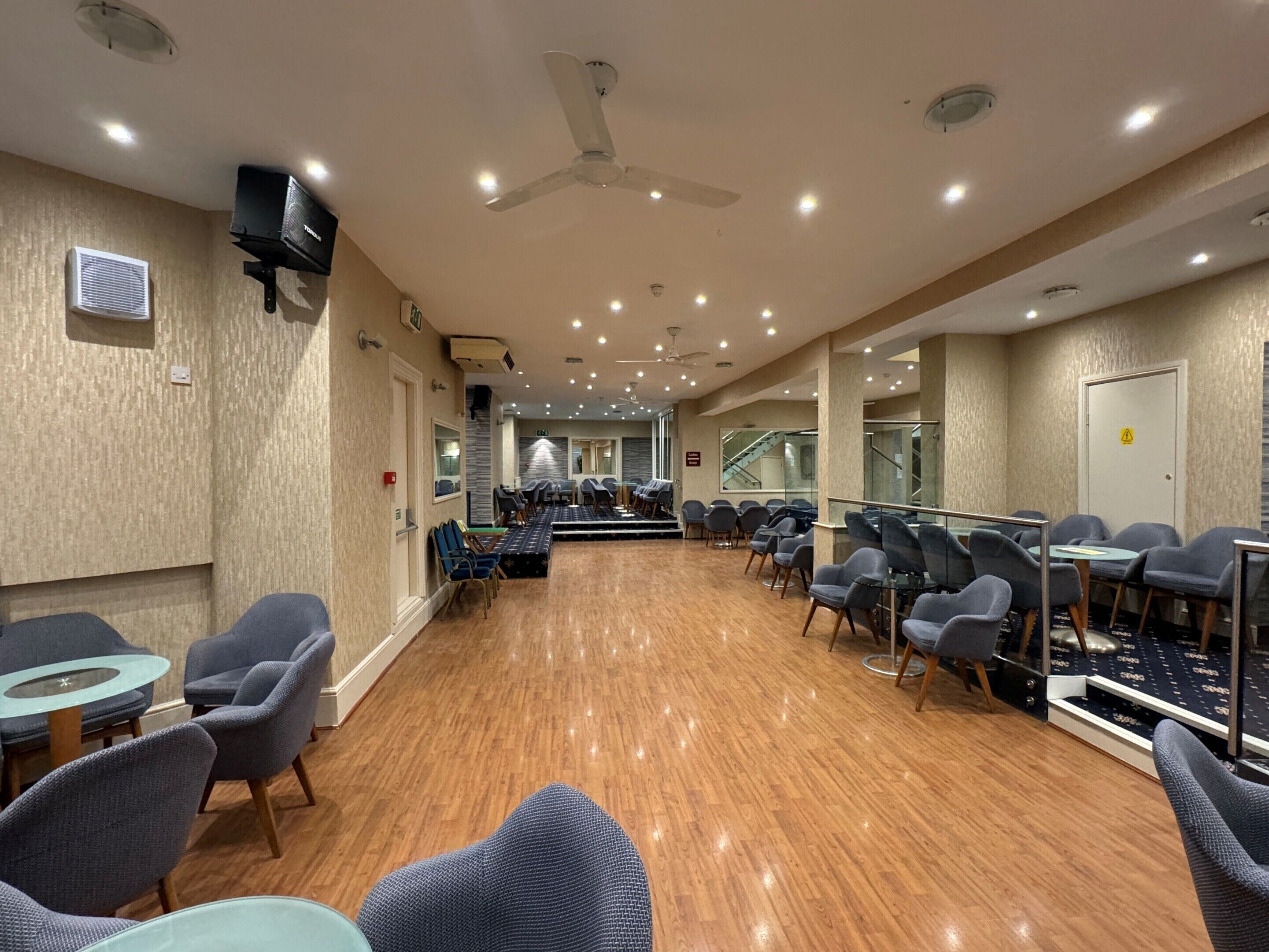 A spacious conference room with rows of chairs, a stage, and a ceiling fan.