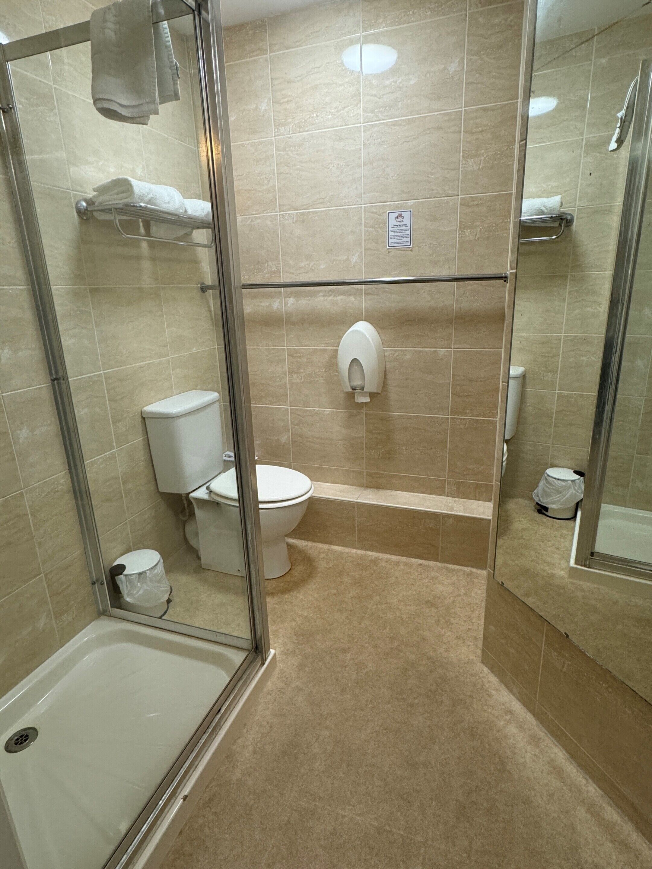 A bathroom with a glass-enclosed shower, a toilet, and a hand dryer.
