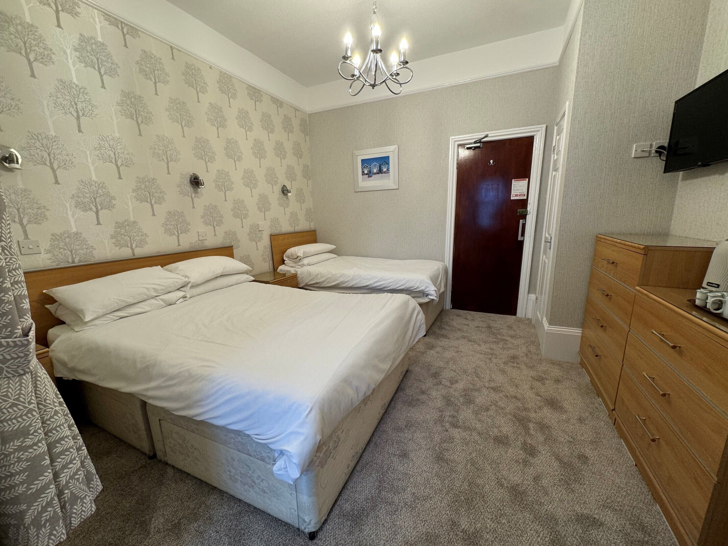 A hotel room with two beds, a wooden dresser, a television, and a door leading to another room.