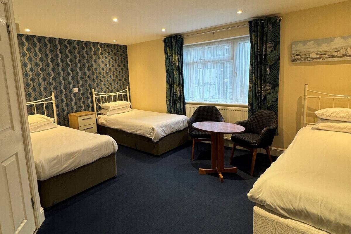 A hotel room with two single beds, a small round table with a chair, and a window with curtains.