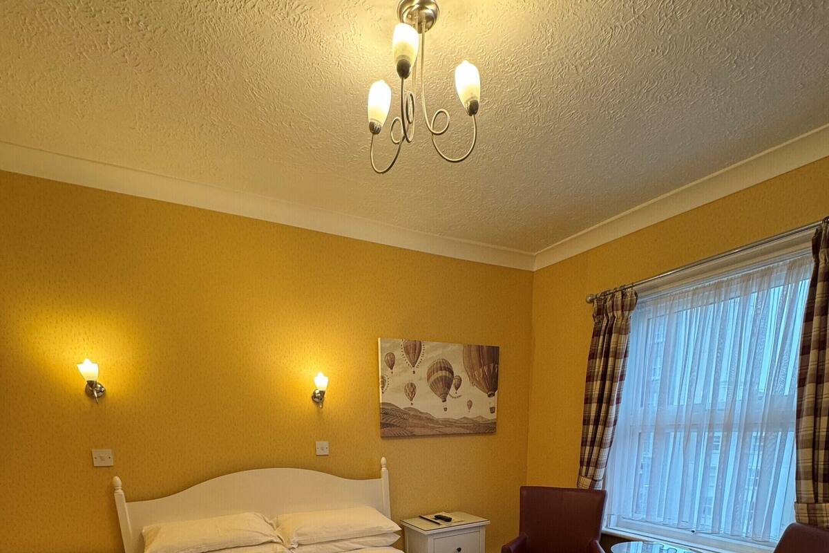 A hotel room with a large bed, a desk with a chair, a small table, and a window with curtains.