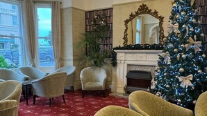 Une pièce dotée d’un tapis à motifs rouges, d’un grand sapin de Noël, d’une cheminée et d’un lustre.