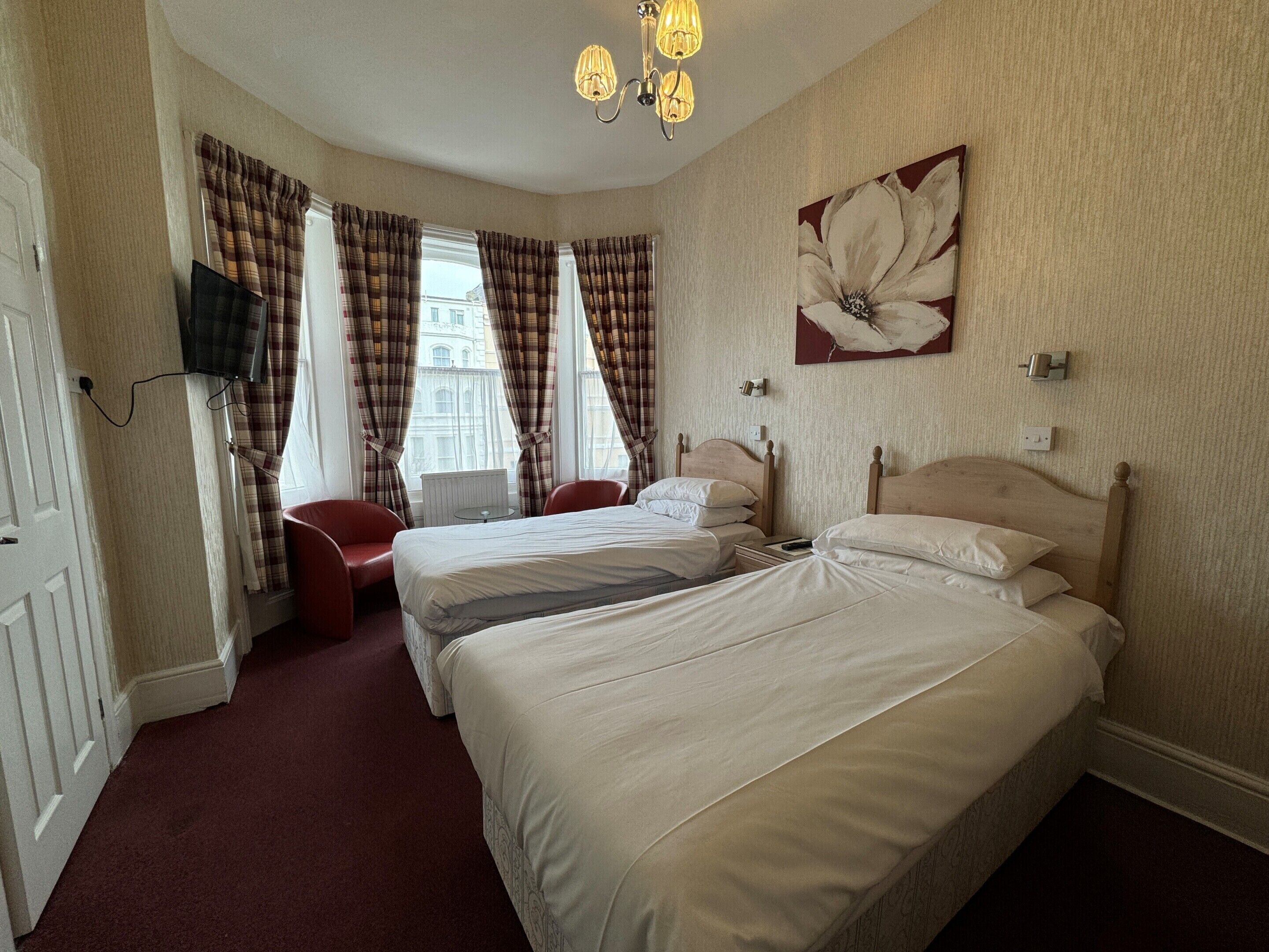 A hotel room with two beds, a red chair, a small table, and a large flower painting on the wall.