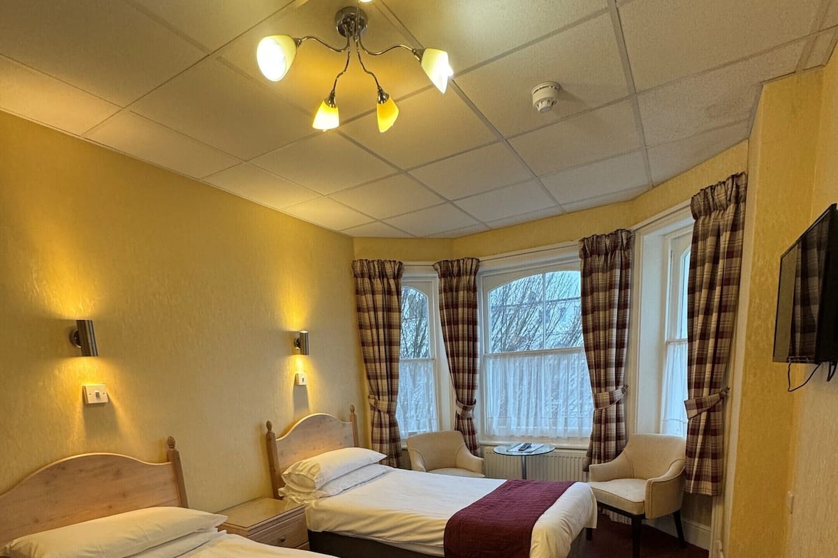 A hotel room with two beds, a chair, a television, and a ceiling light fixture.