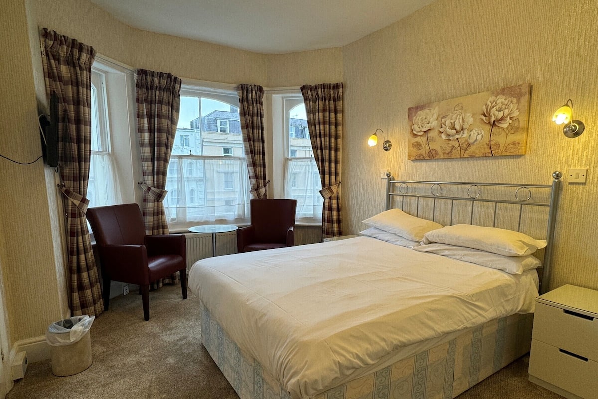 A hotel room with a large bed, two armchairs, a small table, and a painting on the wall.
