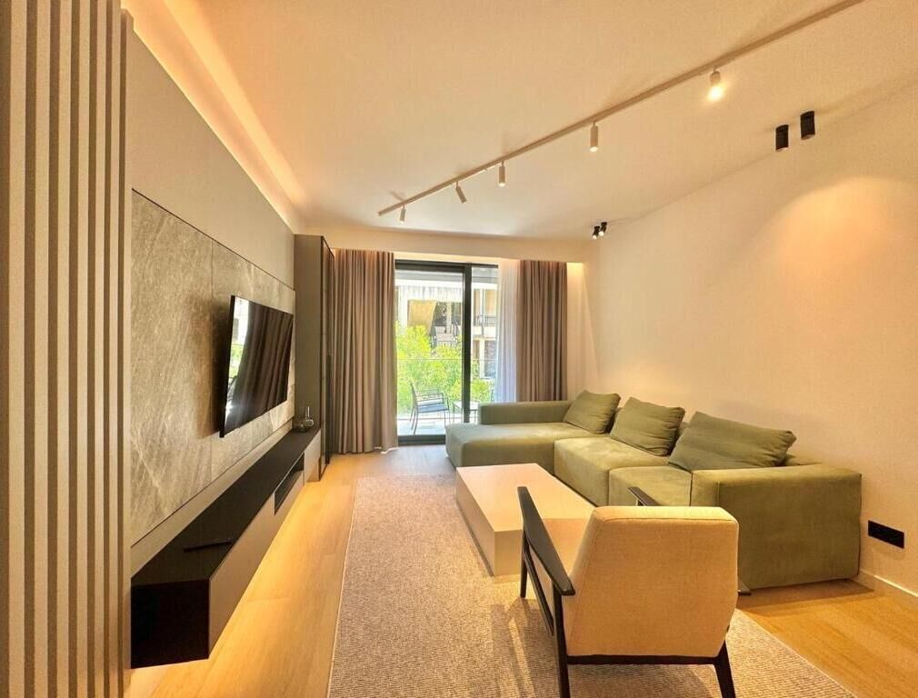 Ein modernes Wohnzimmer mit einer Eckcouch, einem Flachbildfernseher und einem großen Fenster mit Vorhängen.