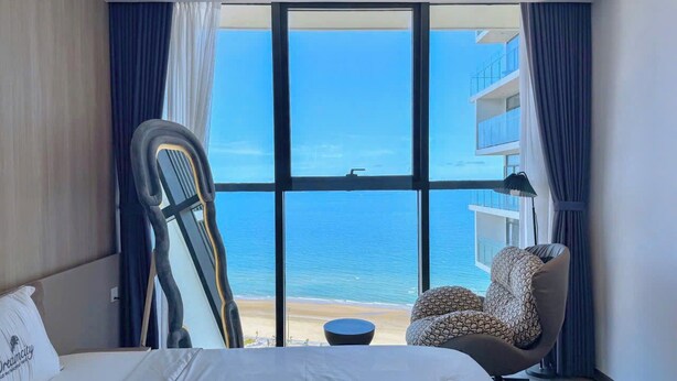 Camera d'albergo con un'ampia finestra vista spiaggia e mare.