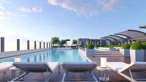 Area piscina sul tetto con poltronne prendisole e una vista aperta sul cielo.