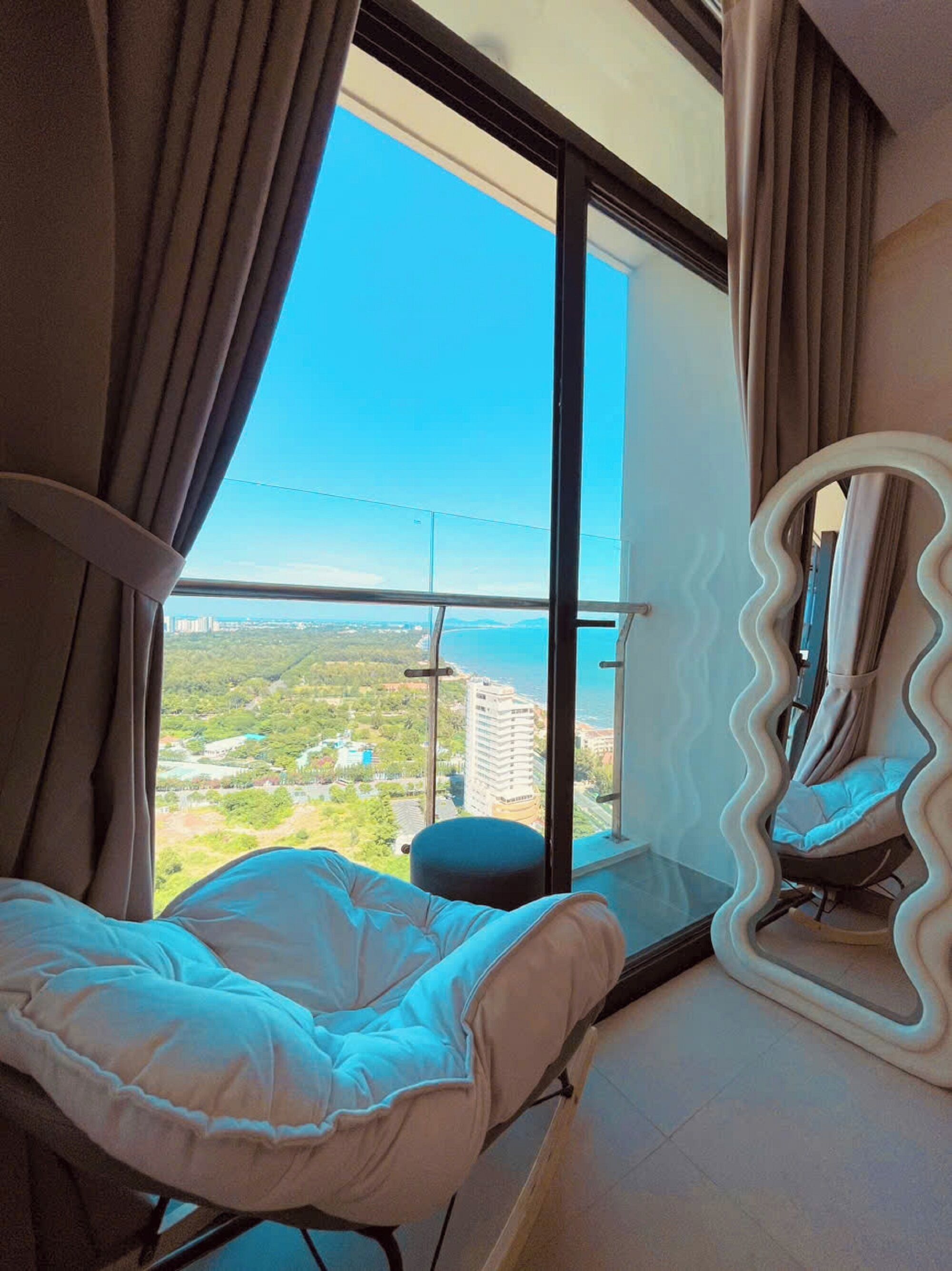 A room with a large window, a bed, a chair, and a mirror.