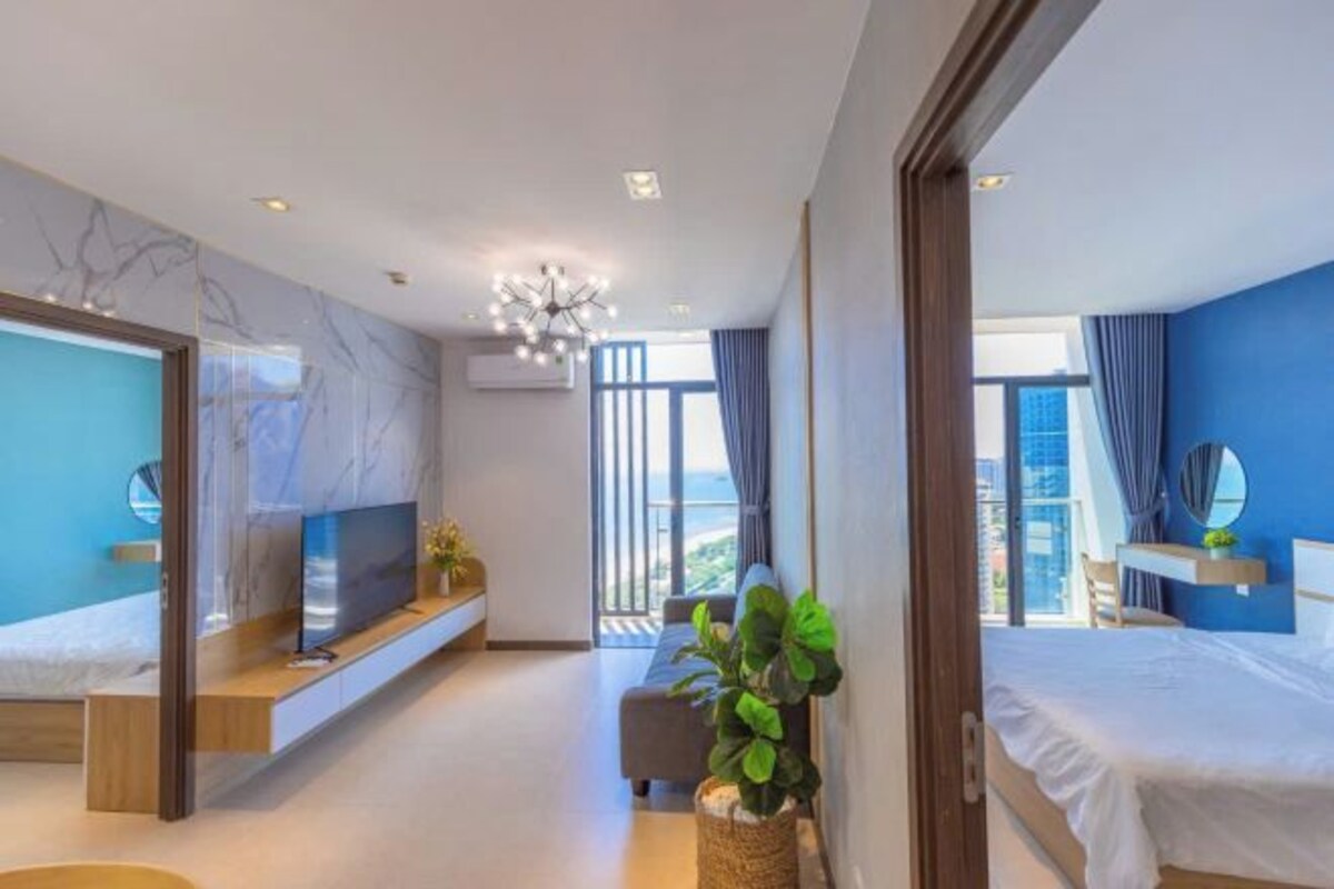 Una habitación de hotel moderna con una cama grande, televisión, balcón con vistas y una lámpara en el techo.