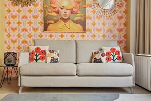 A sofa with floral cushions, a wall with a geometric pattern, and a framed artwork above the sofa.