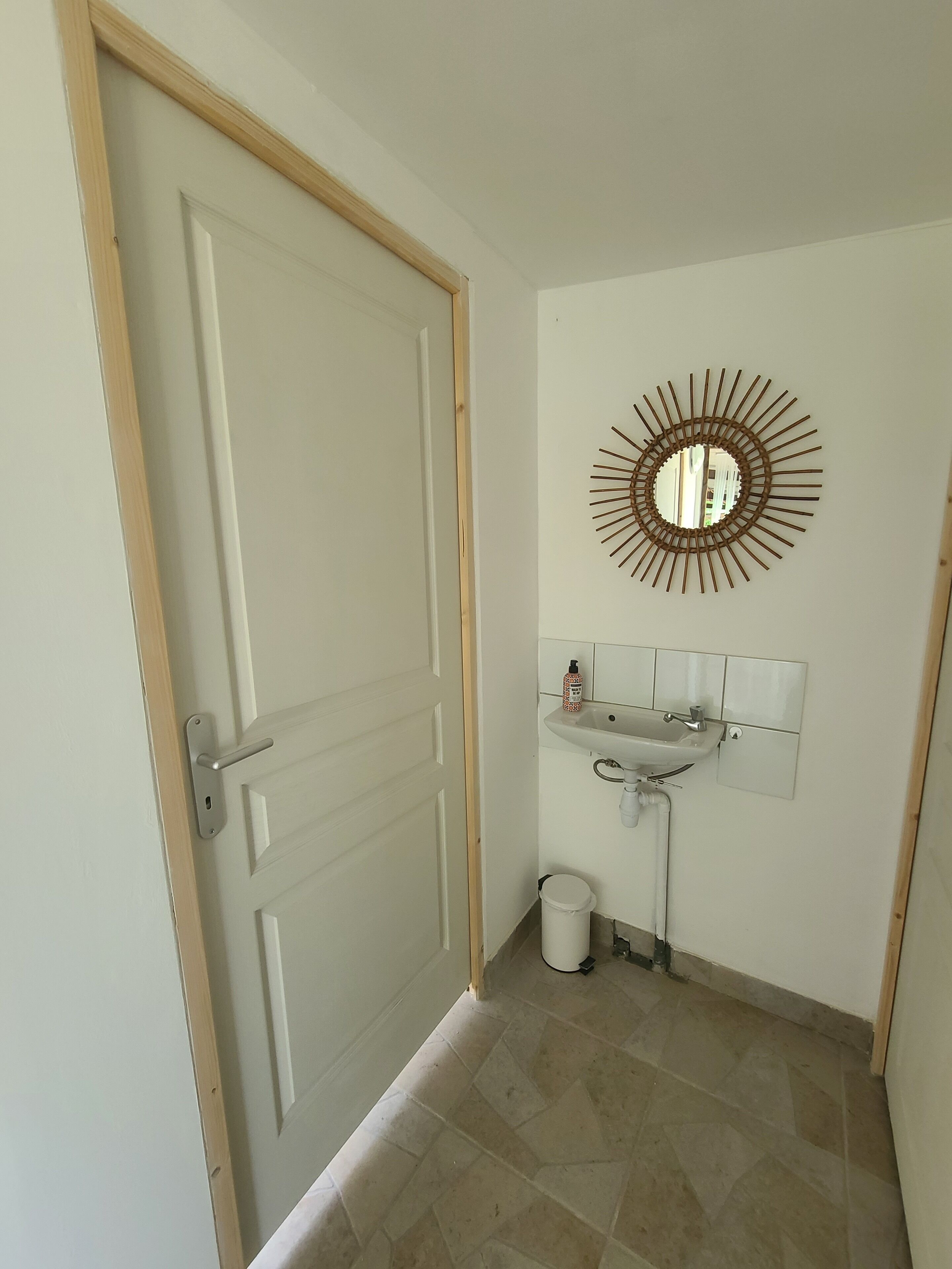 Une salle de bain avec une porte blanche, un lavabo surmonté d’un miroir et une poubelle.