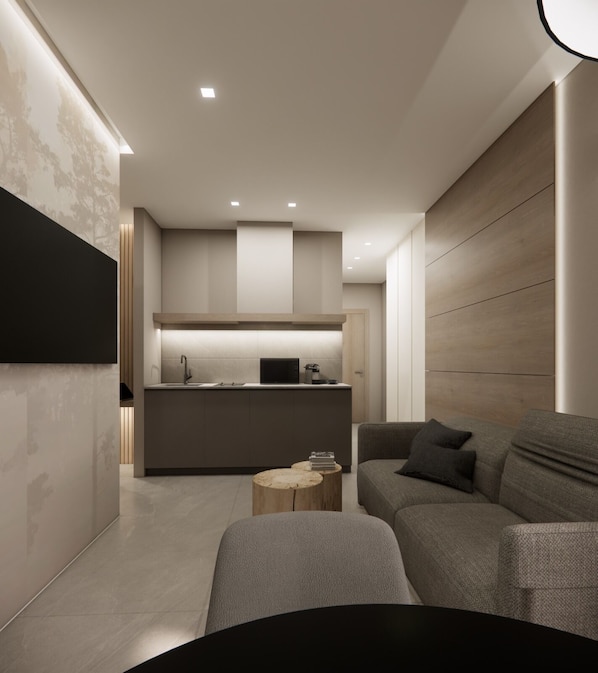 A modern living room with a grey sofa, a round coffee table, and a kitchen area with a central island and built-in appliances.