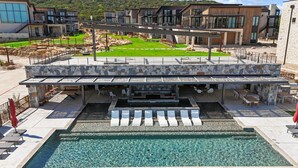 A modern outdoor pool area with a stone deck, lounge chairs, and a covered seating area.