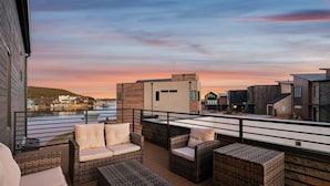 A rooftop terrace with wicker furniture and a view of the city skyline at sunset.