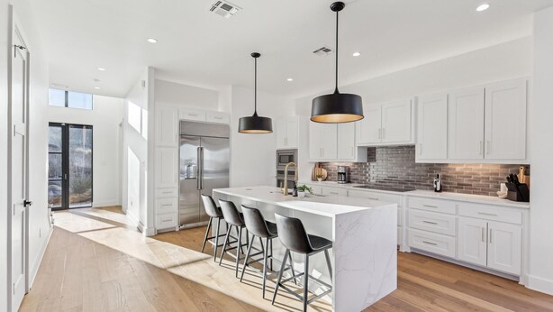 A modern kitchen with white cabinets, a central island with bar stools, and pendant lighting.