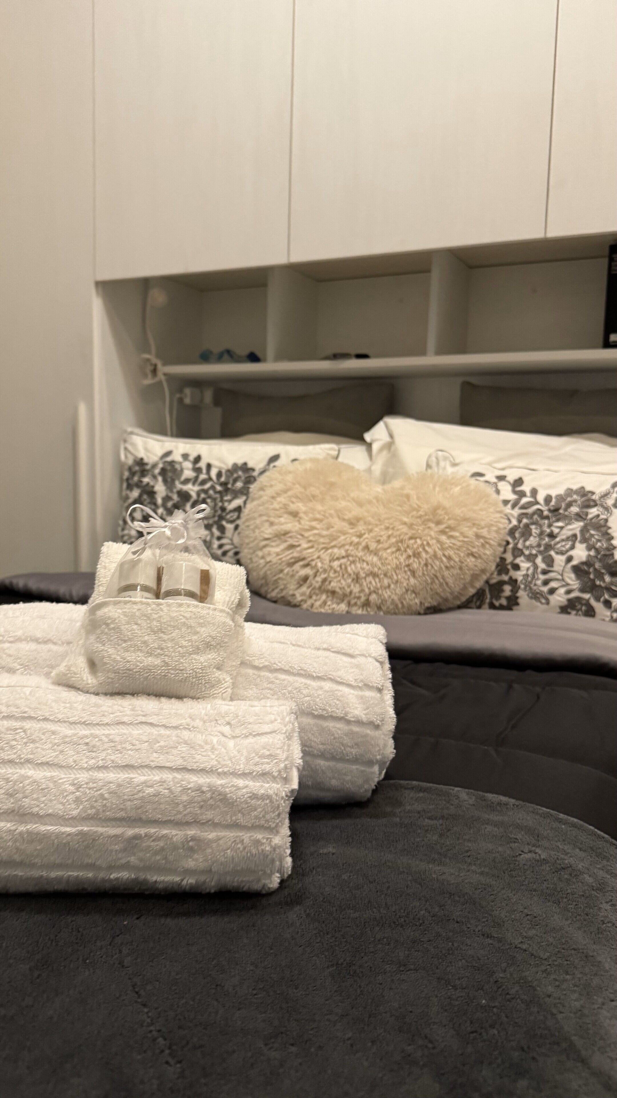 Een keurig opgemaakt bed met witte handdoeken, een zacht kussen en een grijze deken.