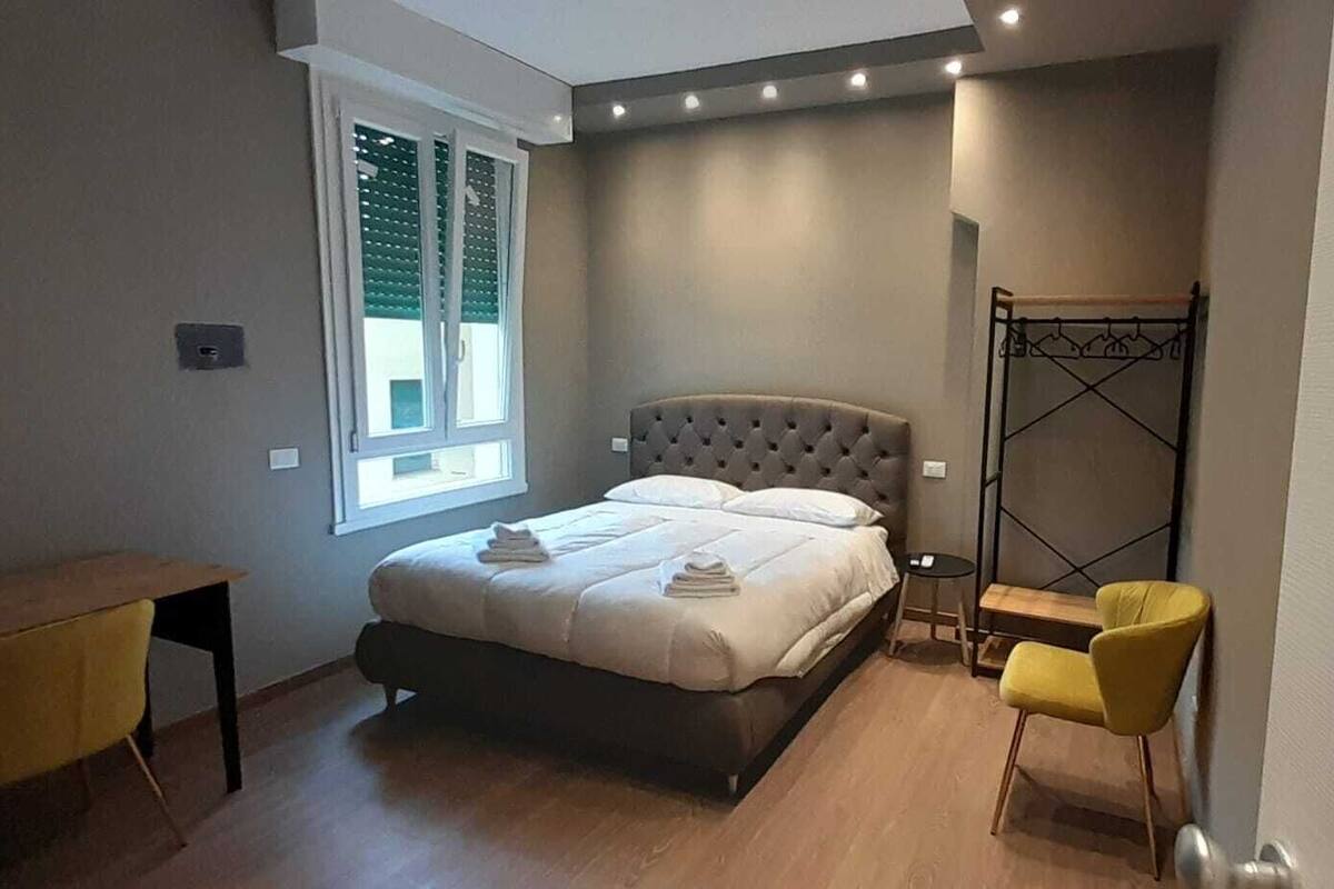 A bedroom with a bed, a small table, a chair, and a window with blinds.