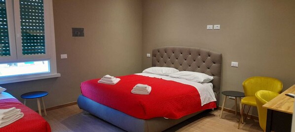 A hotel room with a bed, a small table, a yellow chair, and a window with blinds. - Stazione Tiburtina Roma (Rome)