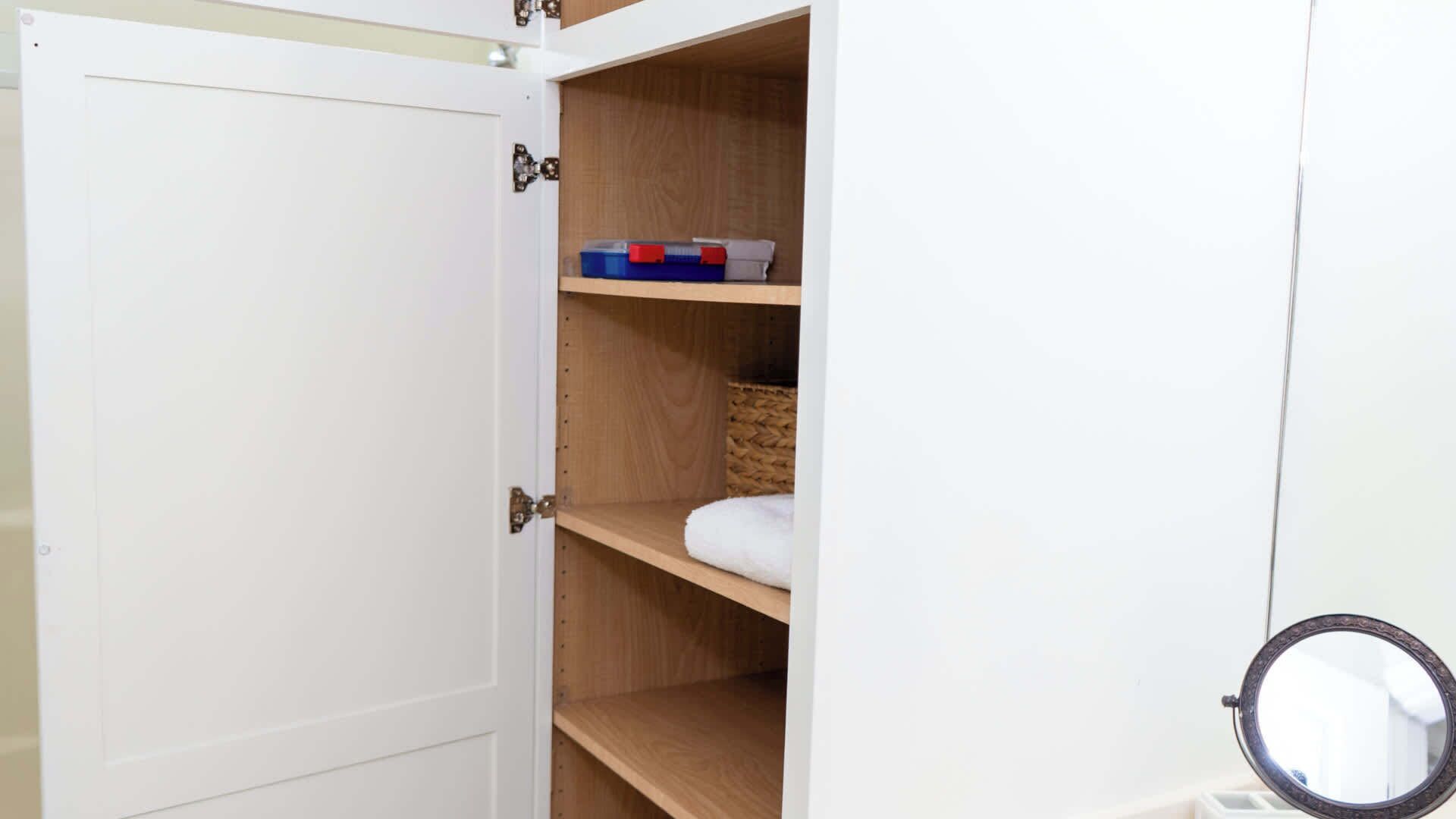 A white wardrobe with a mirror and a shelf with storage boxes.