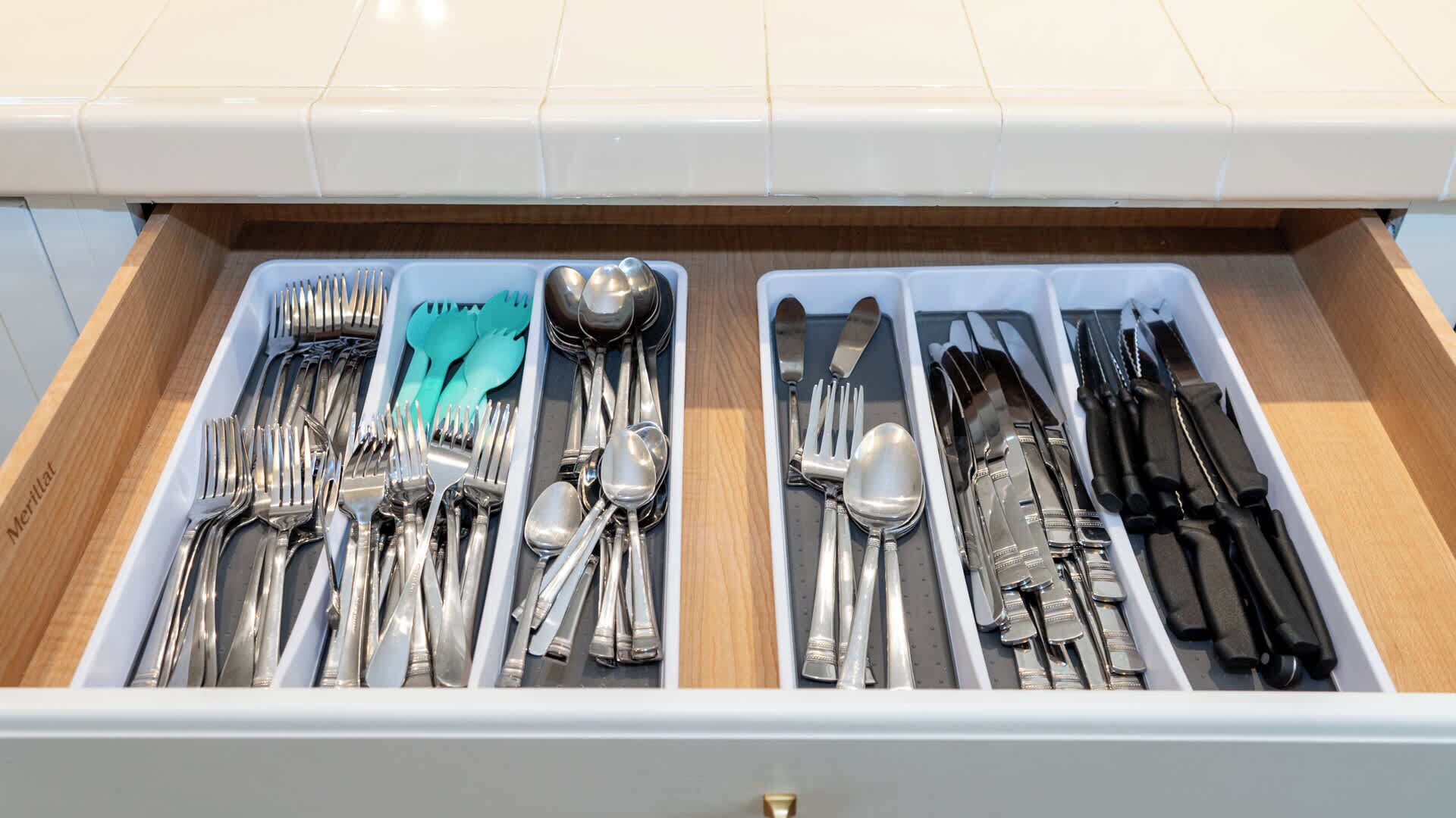 A drawer with neatly organized silverware, including forks, spoons, and knives, divided into two sections.