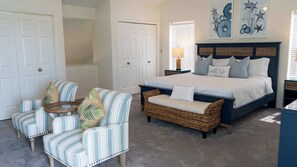 A bedroom with a bed, two armchairs, a bench, and a nightstand with a lamp. - Upscale & Spacious Home - Renovated - Pool (South Padre Island)