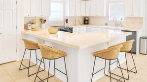 A modern kitchen with white cabinetry, a large island with bar stools, and a coffee maker. - Upscale & Spacious Home - Renovated - Pool (South Padre Island)