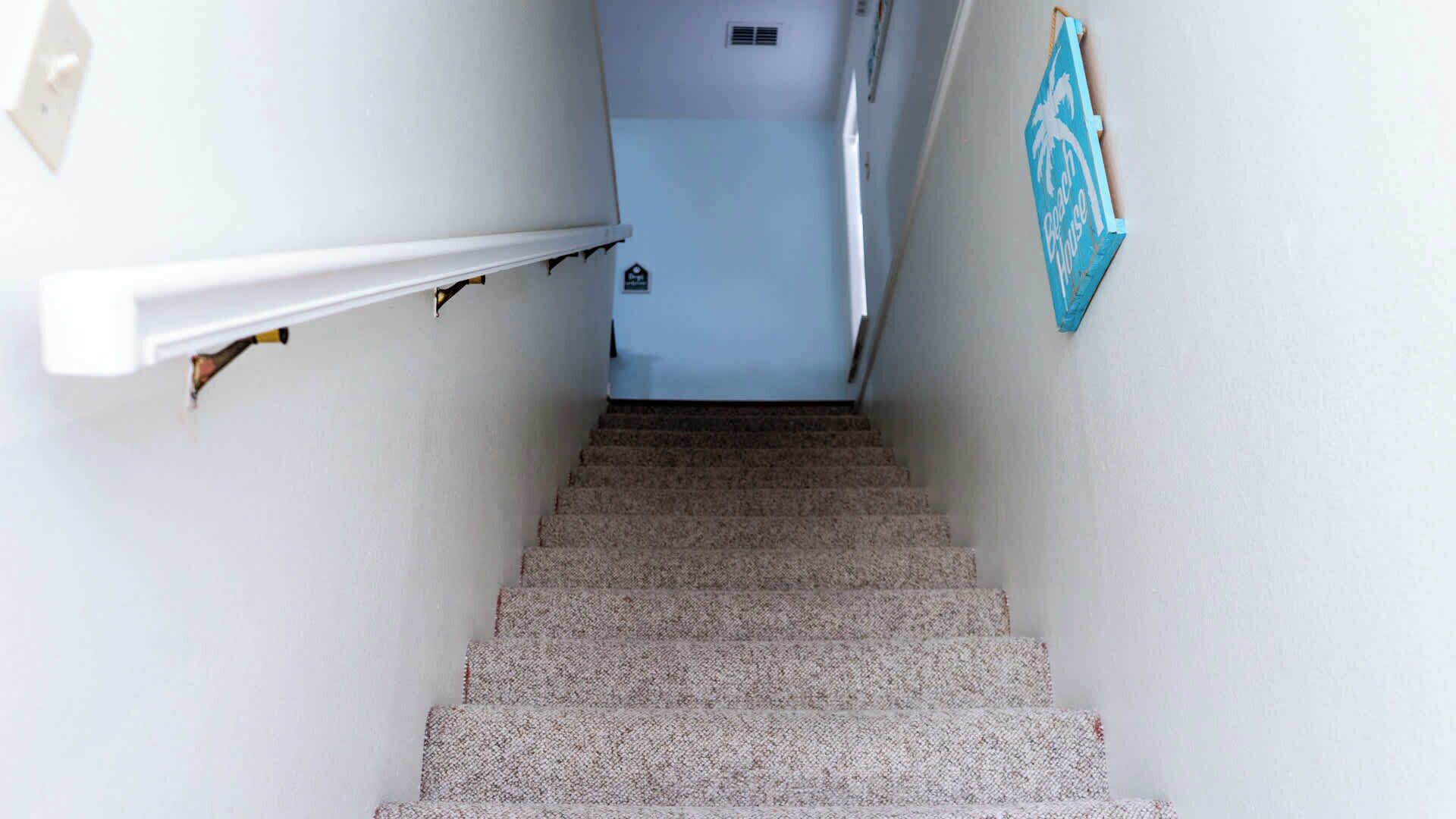 Un escalier recouvert de moquette, avec un mur blanc et un panneau bleu sur le côté droit.