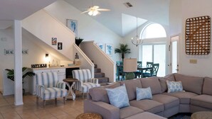 A modern living room with a sectional sofa, striped chairs, a small table, and a staircase leading to a dining area. - Upscale & Spacious Home - Renovated - Pool (South Padre Island)