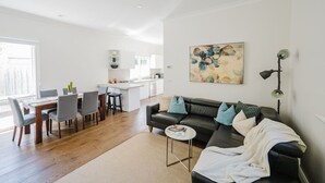 A modern living room with a black leather sofa, a dining table with chairs, and a kitchen in the background. - Navi Home, stay like locals (Yarraville)