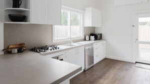 A modern kitchen with white cabinetry, a gas stove, a sink, and a window providing natural light. - Navi Home, stay like locals (Yarraville)