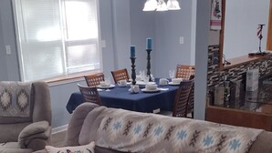 Una sala de estar con un sofá marrón, un plaid estampado y una zona de comedor con una mesa azul.