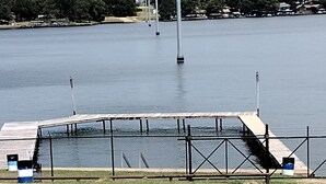 Vista al agua con un muelle, zona ajardinada y una valla.