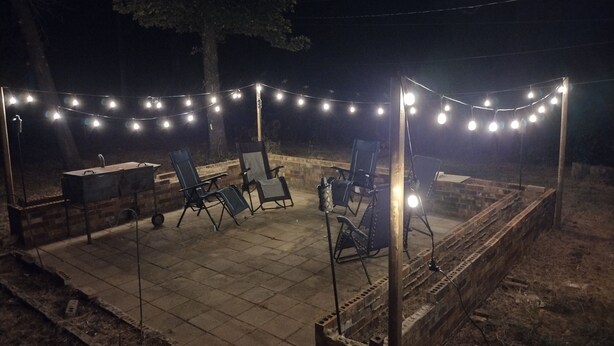 Un espacio de patio al aire libre con luces colgantes, una parrilla y sillas plegables.
