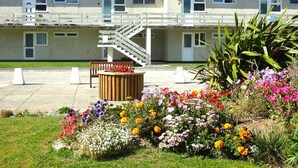 A building with a staircase leading to a balcony, surrounded by a garden with various flowers. - Beachfront apartment with direct beach access! (Perranporth)