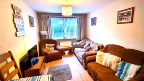 A cozy living room with a brown sofa, a wooden chair, a small table, and a lamp.