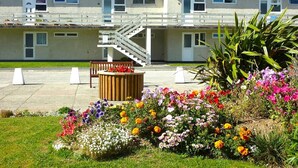 A residential building with a staircase leading to a balcony, surrounded by a garden with various flowers and plants.