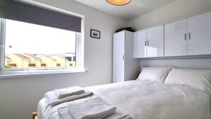 Une chambre à coucher avec un lit, des rideaux blancs, une fenêtre et une armoire.