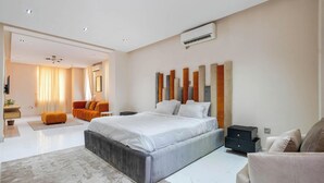 A modern bedroom with a large bed, a sofa, a nightstand, and a wall-mounted air conditioner. - Blue Bell Suites and Apartments (Lekki)