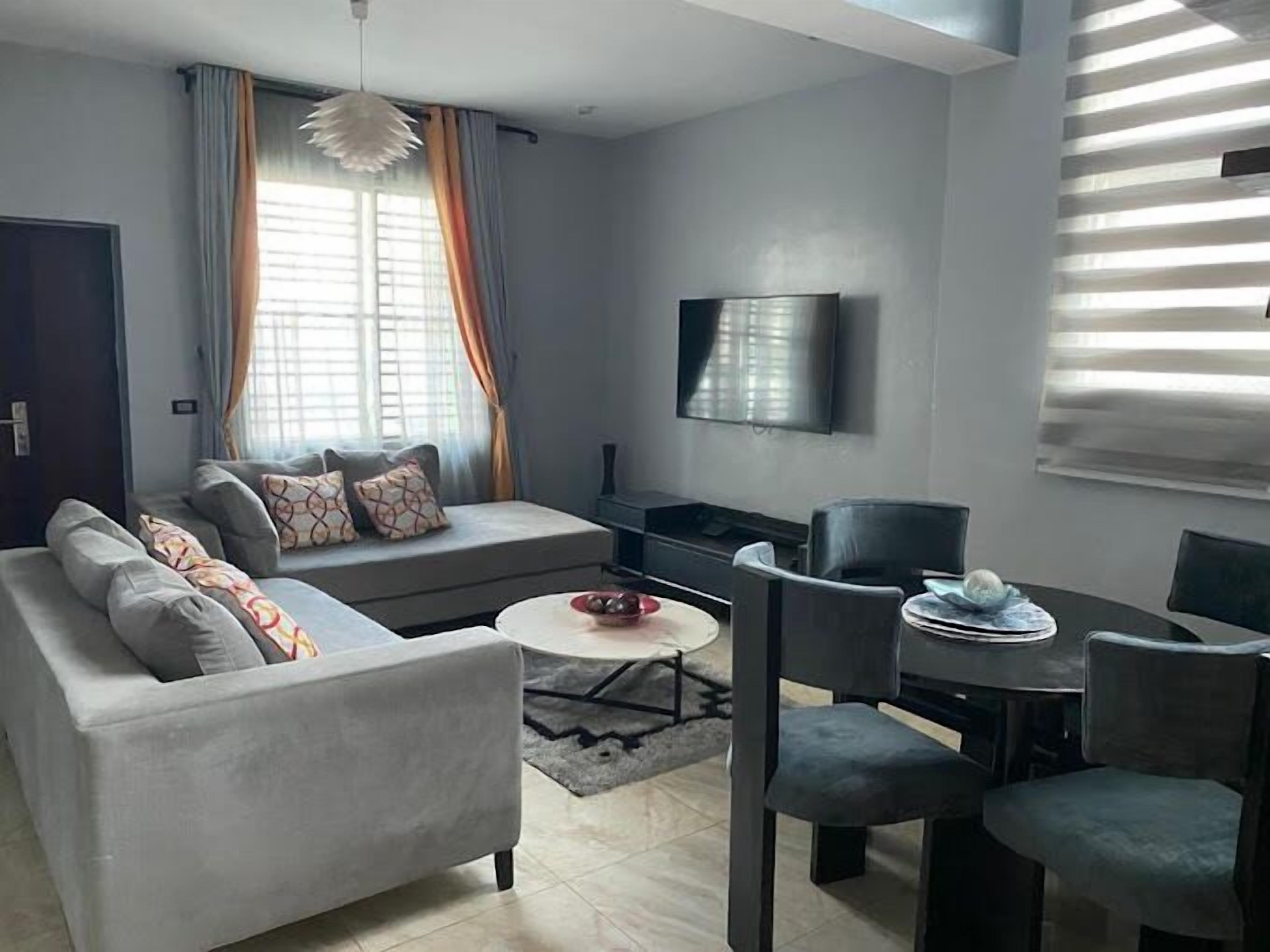 A modern living room with a grey sofa, a small round coffee table, and a TV mounted on the wall.