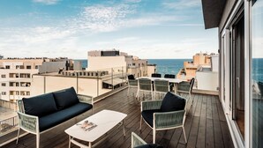 Una terraza en la azotea con mobiliario exterior, vistas al mar y edificios circundantes.