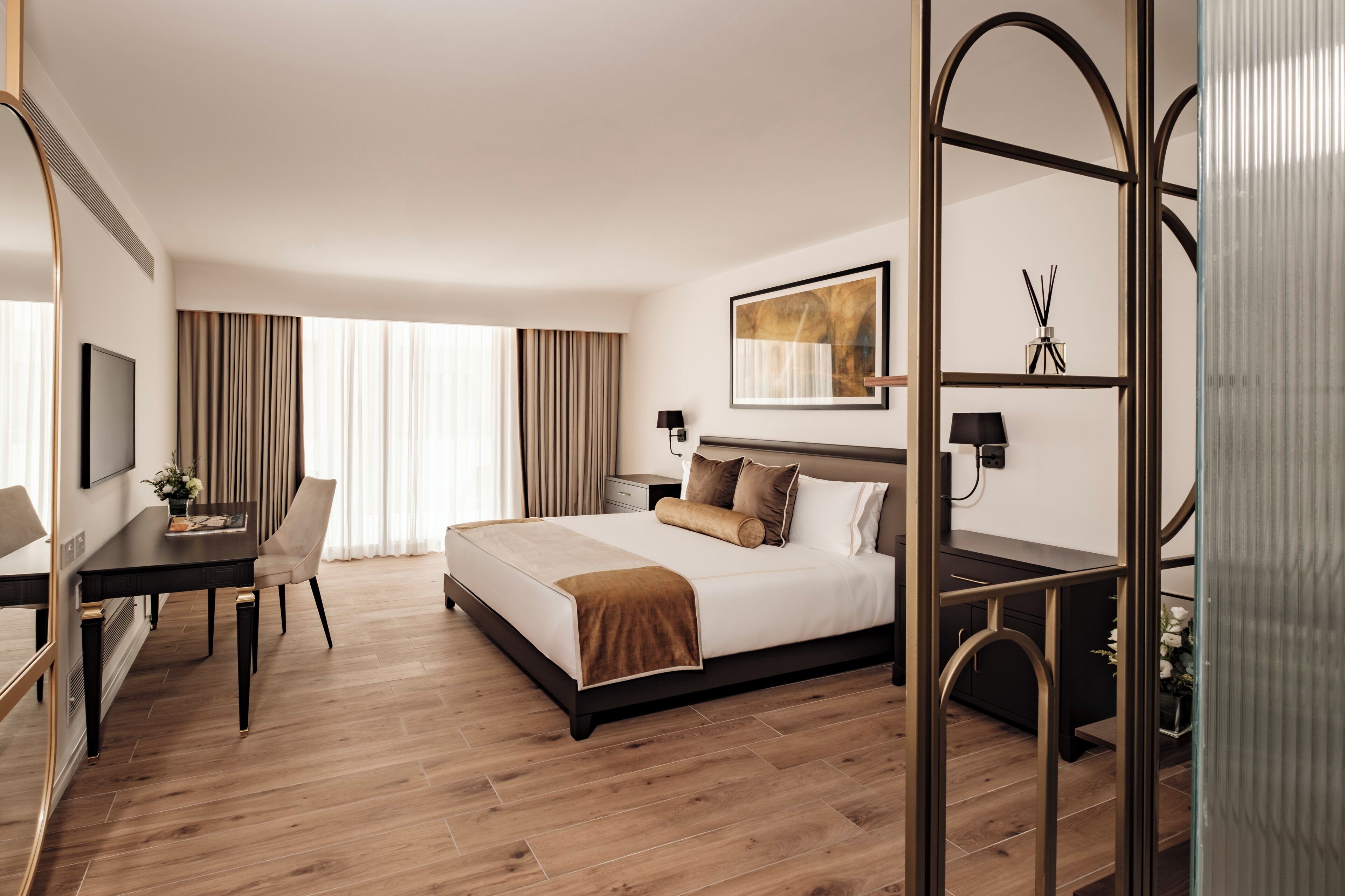 Une chambre d’hôtel avec un lit, un bureau, une chaise, une télévision et une grande fenêtre avec des rideaux.
