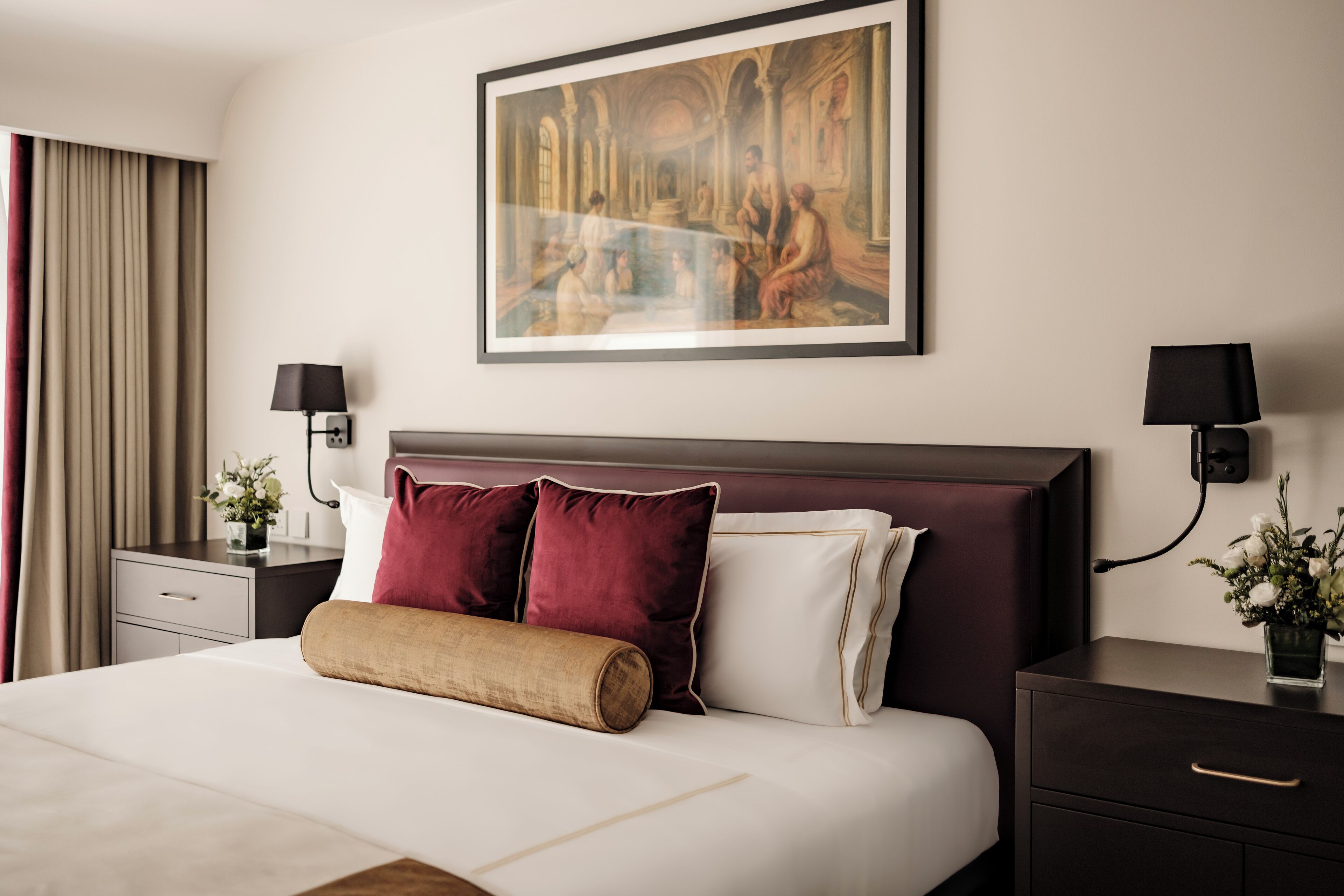 Habitación de hotel con una cama grande, dos mesitas de noche con lámparas, un cuadro enmarcado en la pared y una ventana con cortinas.