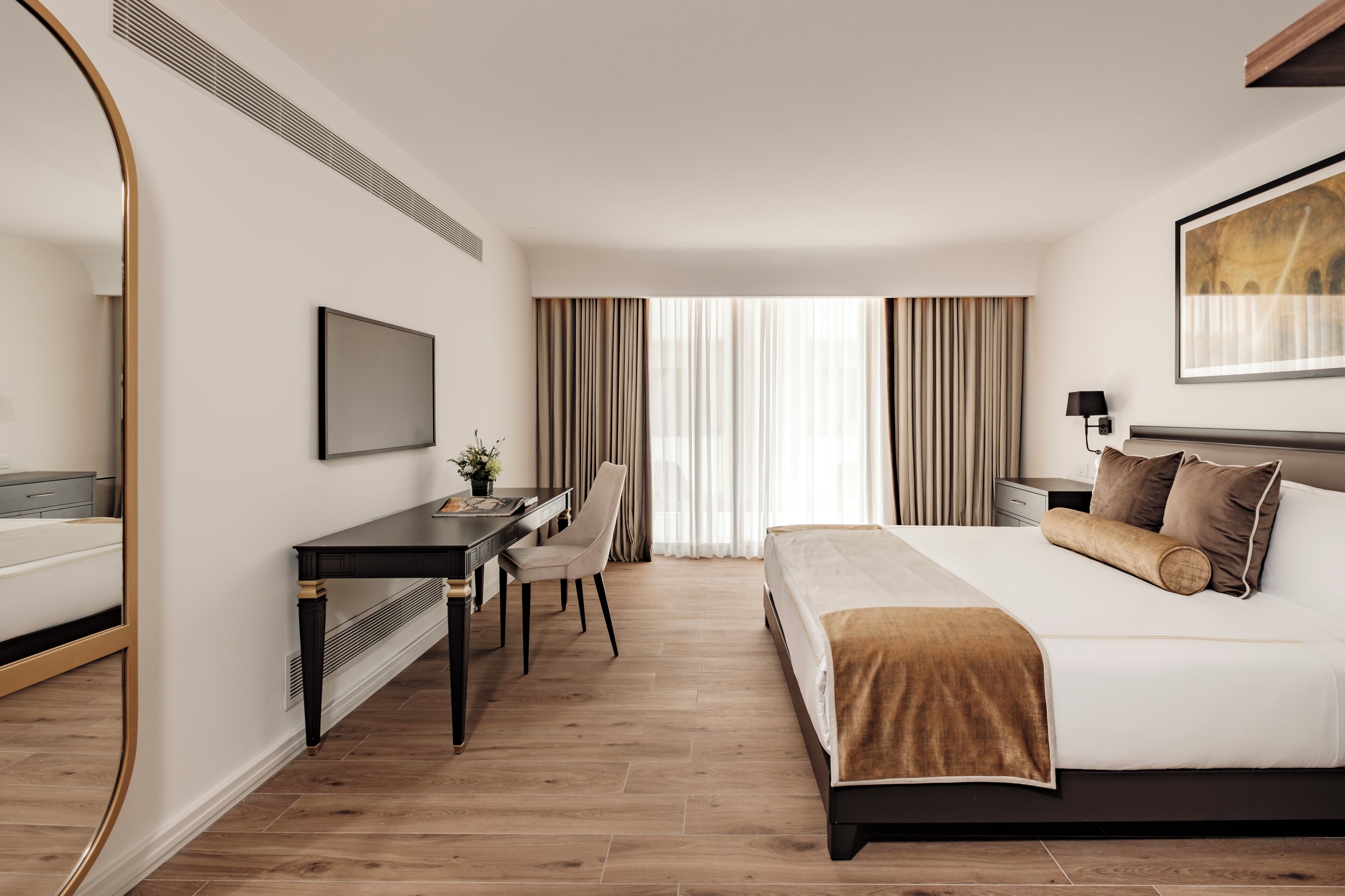 Camera d'albergo con un letto, una scrivania, una sedia, una televisione e una finestra con tende.