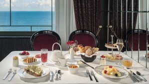 Una mesa lista para el desayuno con diversos platos, vista al mar y sillas de mimbre.